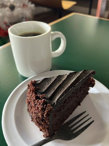 A slice of rich chocolate cake with a cup of black coffee on a green table.