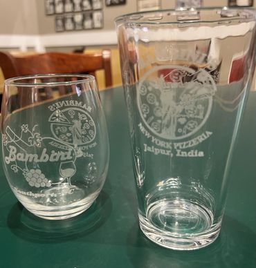 Two clear glasses with etched logos from Bambini's and New York Pizzeria Jaipur, India.