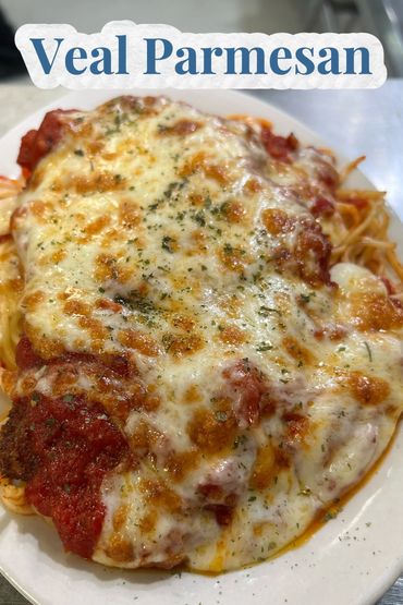 Close-up of veal parmesan with melted cheese and tomato sauce on a white plate.