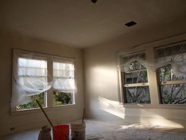 Room under renovation with windows covered in plastic sheets.