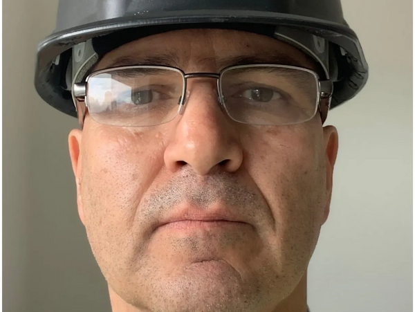 Close-up of a man wearing glasses and a black safety helmet.