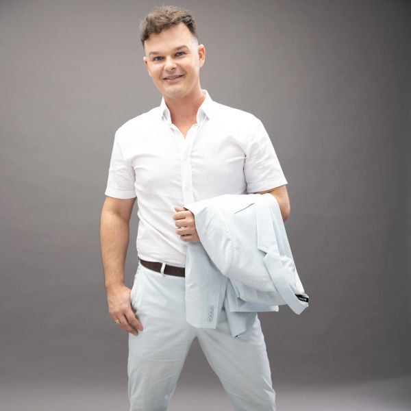 Smiling man in white shirt holding a light blue jacket.