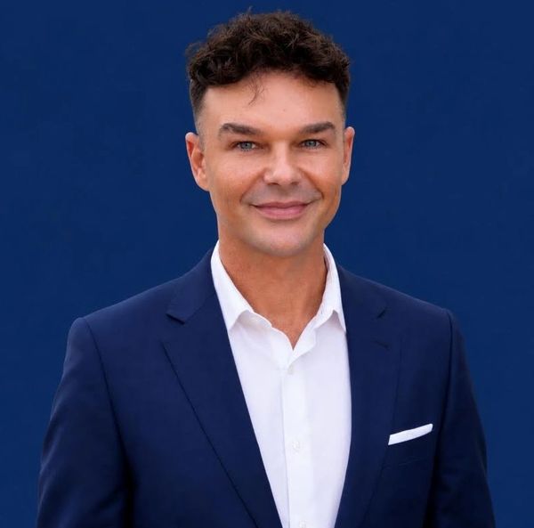 Man in blue suit smiling against a blue background.