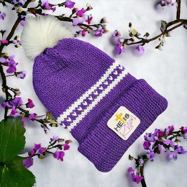 Purple knit beanie with a white pom-pom and floral background.