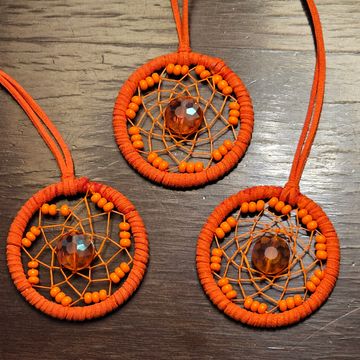 Three orange dreamcatchers with beads and central gems on a wooden surface.