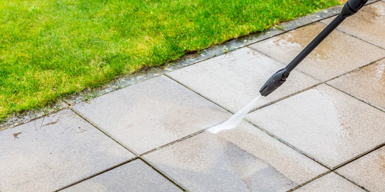 Pressure washing a tiled patio near green grass.
