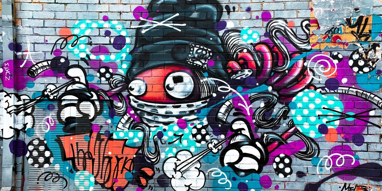 Colorful street art of a whimsical character with big eyes and a beanie on a brick wall.