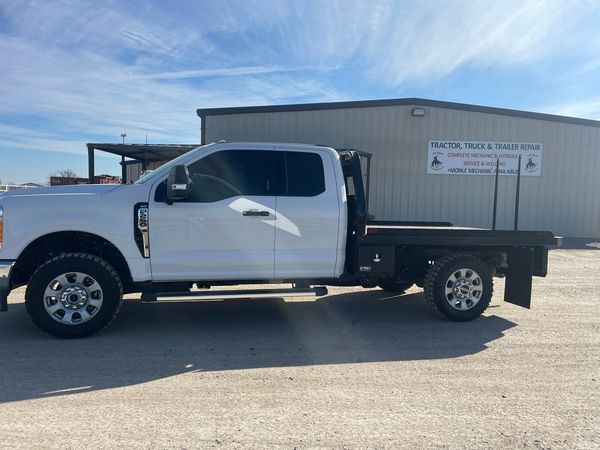 White flatbed truck parked outside repair shop.