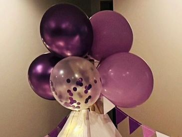 Bunch of purple and transparent balloons with confetti inside, decorating a corner.