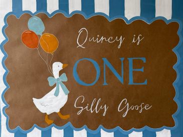A decorative sign celebrating Quincy's first birthday with a silly goose theme.