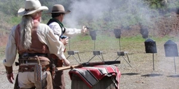 Two cowboys shooting at metal targets on a range.