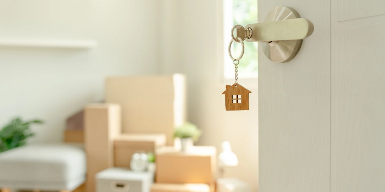 House key with wooden house keychain hanging on door handle.