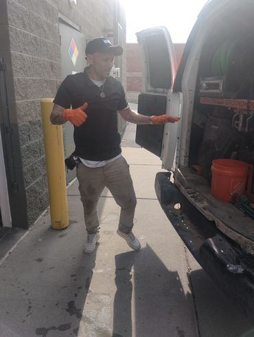 Man wearing orange gloves stands near an open van door.
