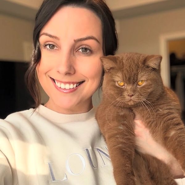 Woman smiling and holding a serious-looking brown cat.