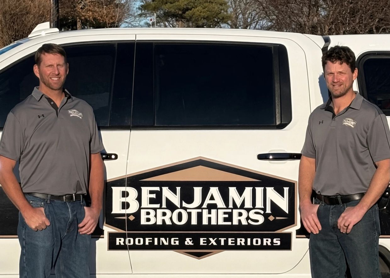 Two men in gray shirts stand beside a white truck with a Benjamin Brothers Roofing & Exteriors logo.