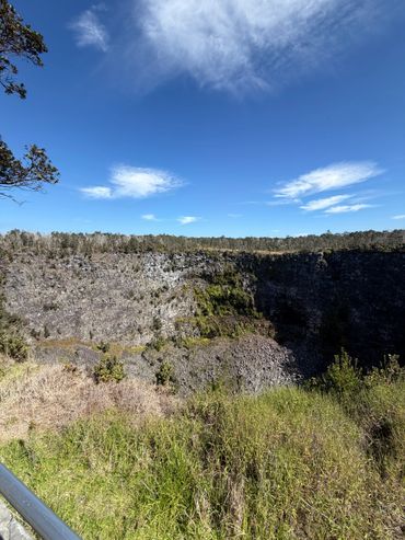 A large rocky crater surrounded by greenery under a clear blue sky.