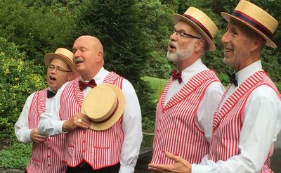 Four men in striped vests and straw hats singing outdoors.