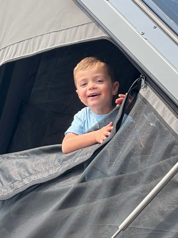 Smiling boy peeks out from a tent zipper.
