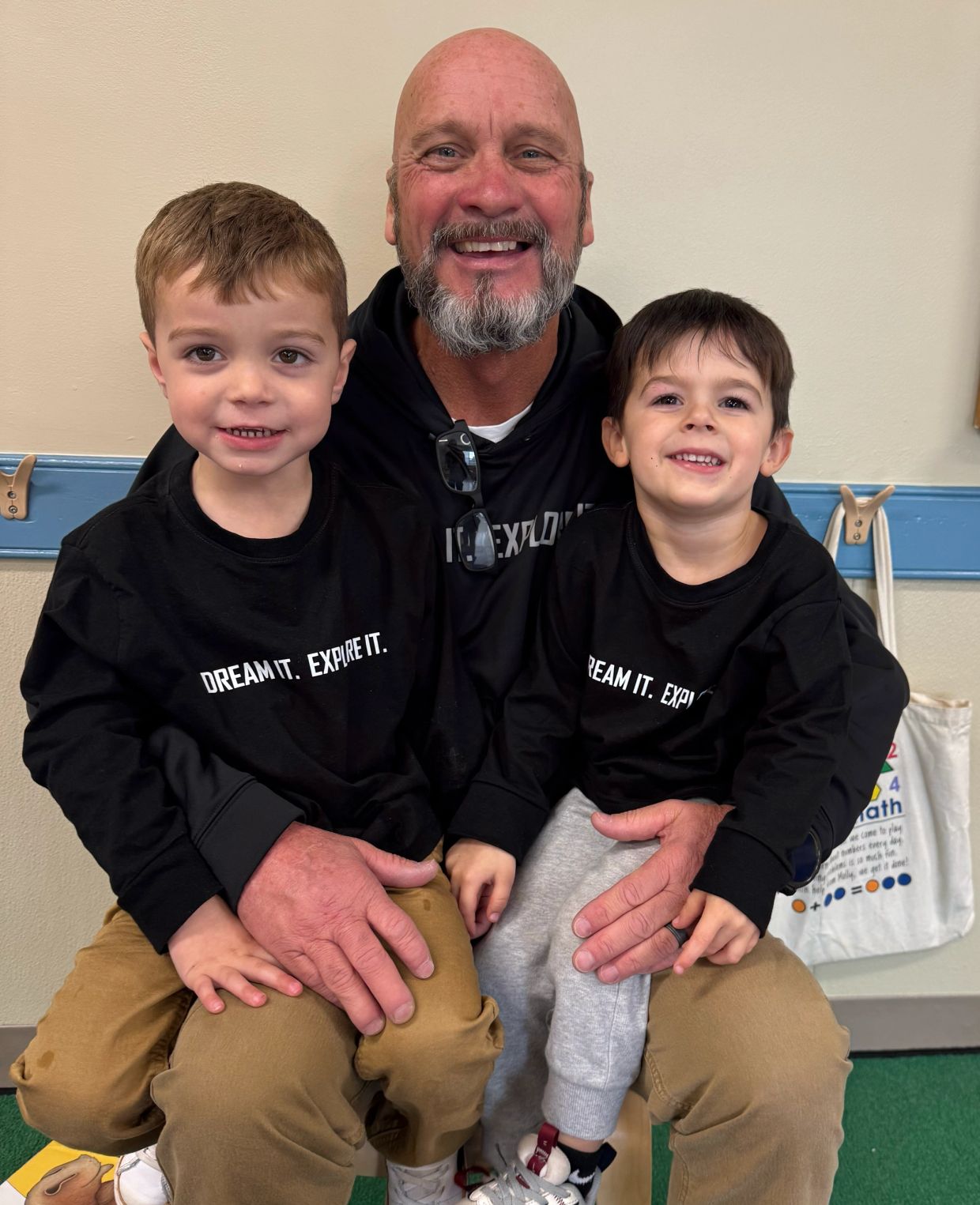 Smiling man with two young boys wearing matching "Dream It. Expire It." shirts.