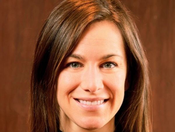 Smiling woman with long brown hair in a black top against a wooden background.