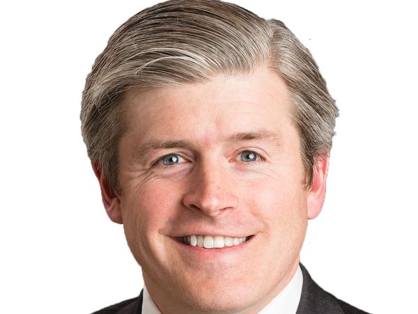 Smiling man in suit with red patterned tie against white background.