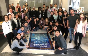A group of team members showing off the collaborative mural they made together