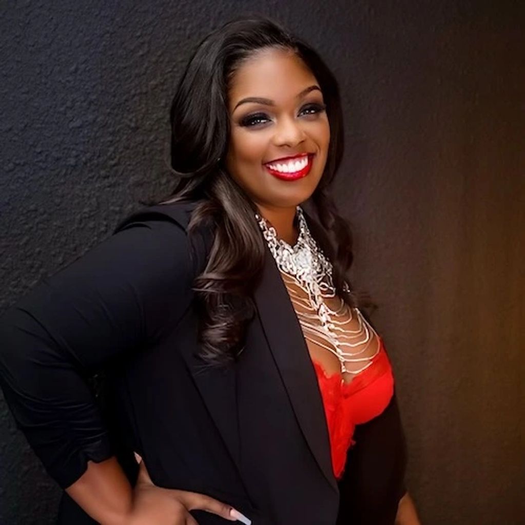 Confident woman in black blazer and red top, smiling brightly against a dark background.
