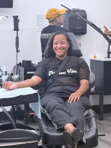 A smiling woman getting a tattoo in a studio with a tattoo artist in the background.