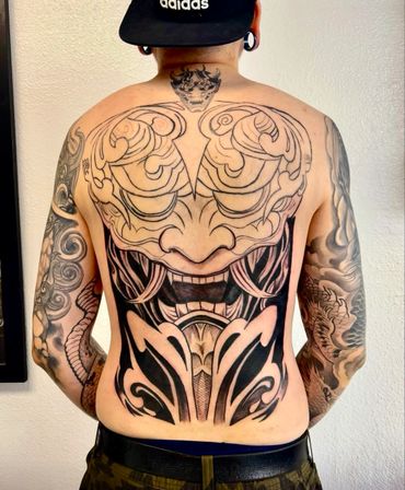 Intricate full-back tattoo with tribal and demon mask designs.