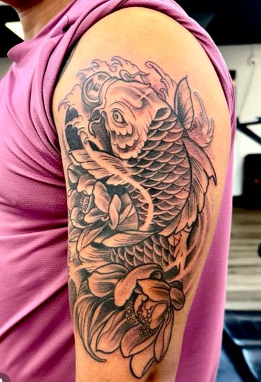 Black and grey koi fish tattoo with floral and wave designs on upper arm.