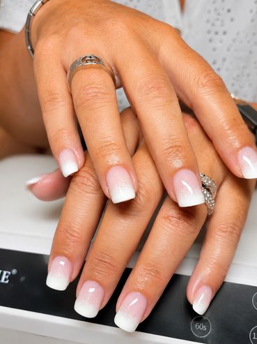 Hands with elegant pink to white ombre nails and silver rings.