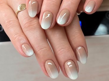 Hands with nude to white ombre nails and rings.