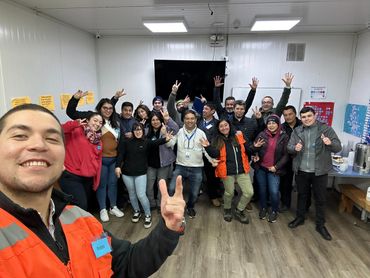 A group photo of smiling people making peace signs indoors.