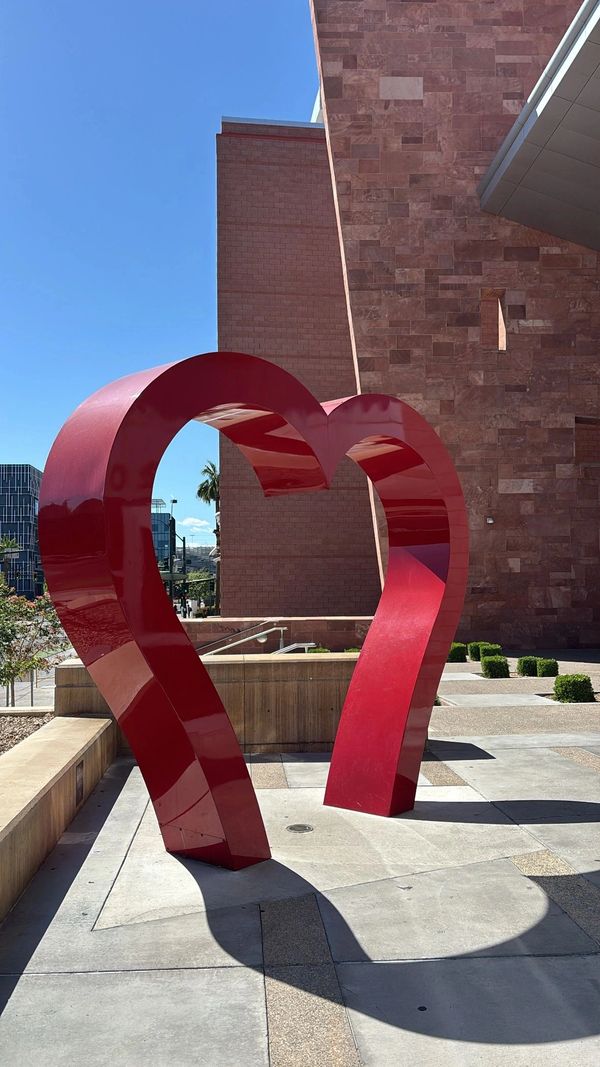 A large red heart-shaped sculpture outdoors against a building.