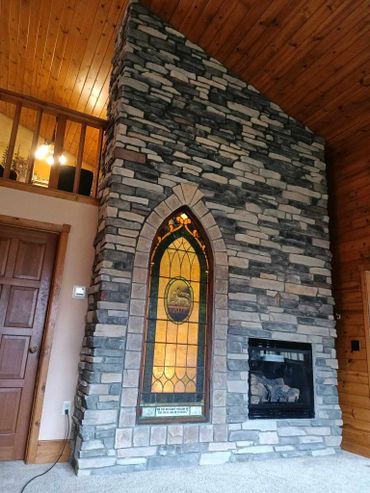 Stone fireplace with stained glass window feature in a wooden cabin interior.