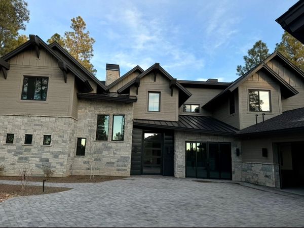 Modern stone and wood house with large windows and a paved driveway.