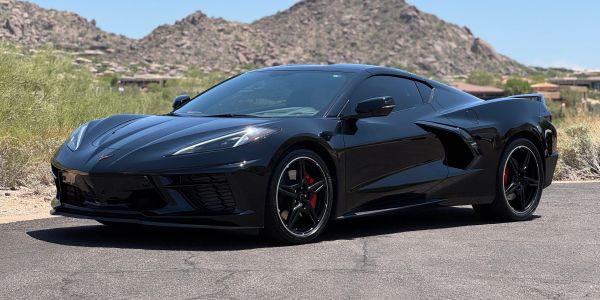 Sleek black sports car parked on a desert road with mountains in the background.