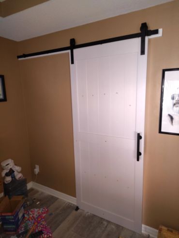White sliding barn door with black hardware on brown wall.