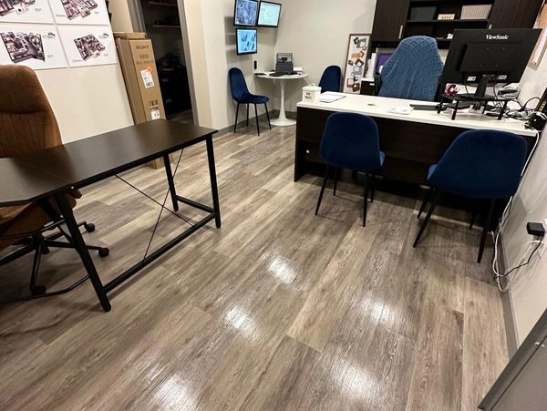 Modern office with wooden flooring, blue chairs, and multiple monitors on the wall.