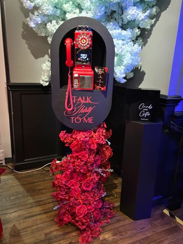 Decorative vintage red phone booth with floral base and 'Talk Stay To Me' sign.