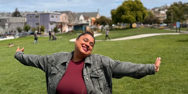 A cheerful person posing outdoors with arms outstretched.