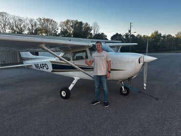 Man giving thumbs up standing next to a small white airplane on a runway.