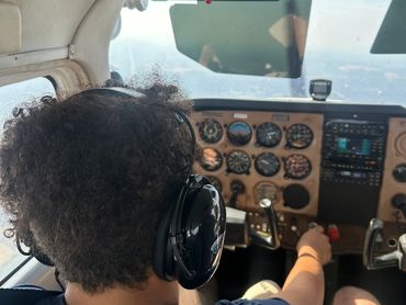 Person wearing headphones piloting a small airplane cockpit.