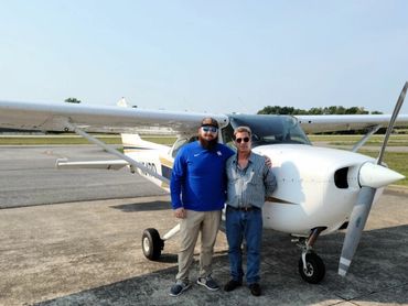 Two men standing beside a small white airplane on a sunny day.