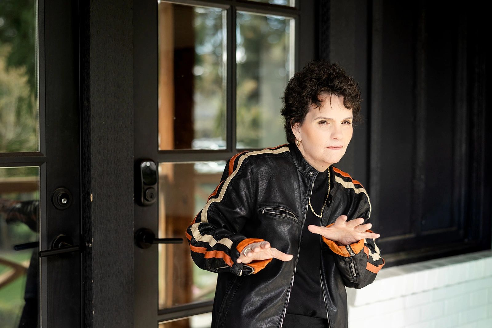 Person in a black leather jacket striking a playful pose near a glass door.