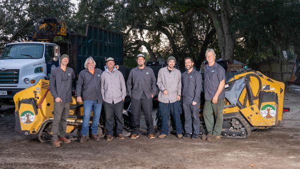 A group of eight workers standing in front of yellow machinery and a truck.