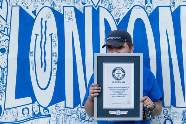 Man holding a framed Guinness World Record certificate in front of a London mural.