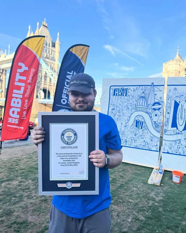 Man proudly holding a Guinness World Records certificate outdoors with event banners behind.