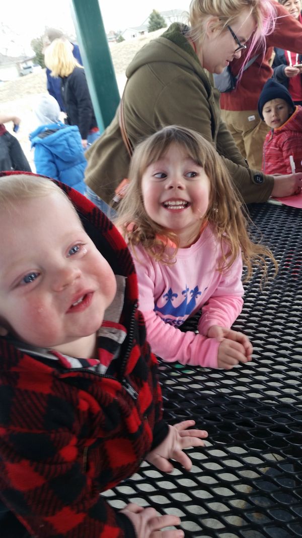 Two happy children leaning on a black metal picnic table outdoors.