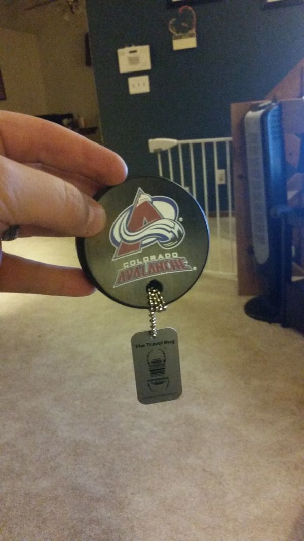 Hand holding a Colorado Avalanche hockey puck keychain indoors.